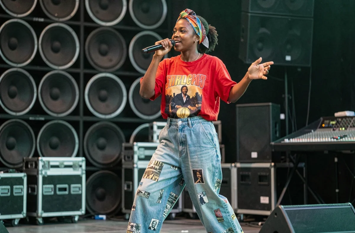 Artiste reggae féminine sur scène avec microphone sans fil, tenue colorée et énergie scénique expressive lors d'un concert